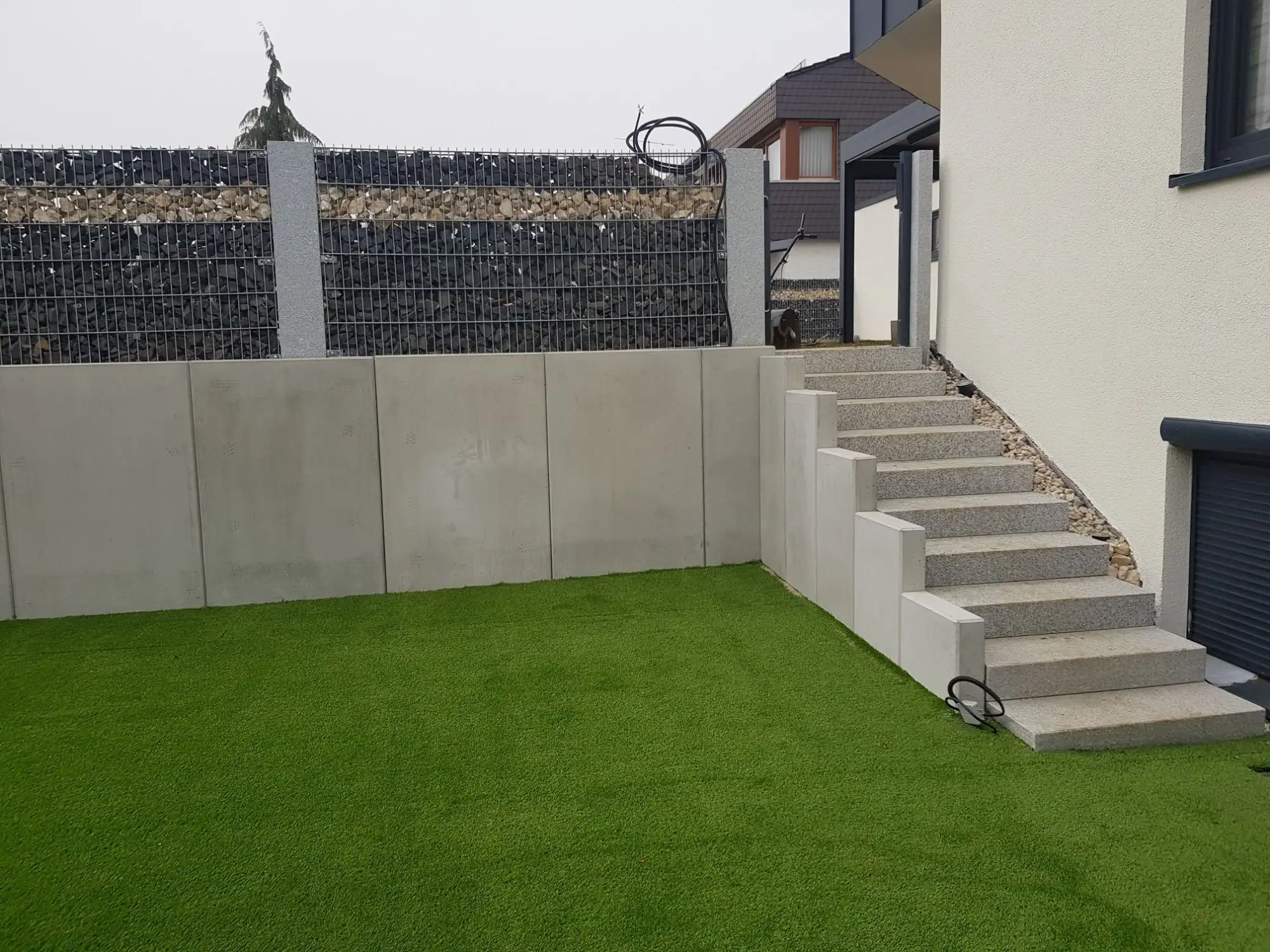 Stützmauer aus Betonwinkeln mit Gabionen, Außentreppe aus Blockstufen am Haus